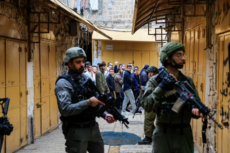 Los israelíes pasan junto a las tropas que hacen guardia durante una gira semanal de colonos en Hebrón, en la Ribera Occidental ocupada por Israel, el 13 de diciembre de 2025. REUTERS/Mussa Qawasma