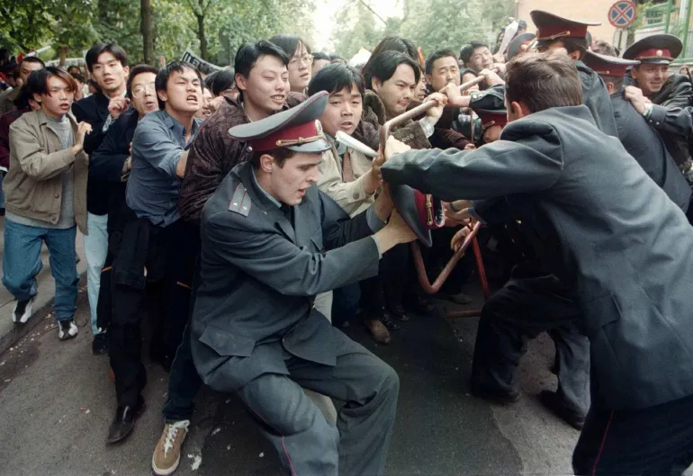 Estudiantes chinos atraviesan una fila de agentes de policía en la embajada de Estados Unidos en Kiev, Ucrania, el 11 de mayo de 1999, durante su protesta contra el bombardeo de la embajada de China en Belgrado.