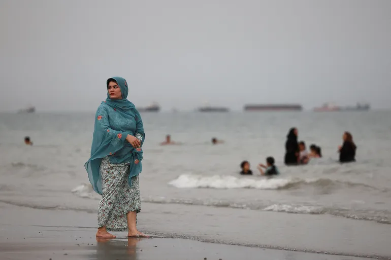 Una mujer iraní camina por la playa mientras los barcos en el Estrecho de Ormuz son visibles cerca de la playa de Bandar Abbas, Irán.