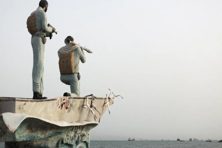 Una estatua de miembros militares iraníes se alza mientras se ven barcos en el Estrecho de Ormuz cerca de la playa de Bandar Abbas, Irán, el 22 de mayo de 2026.